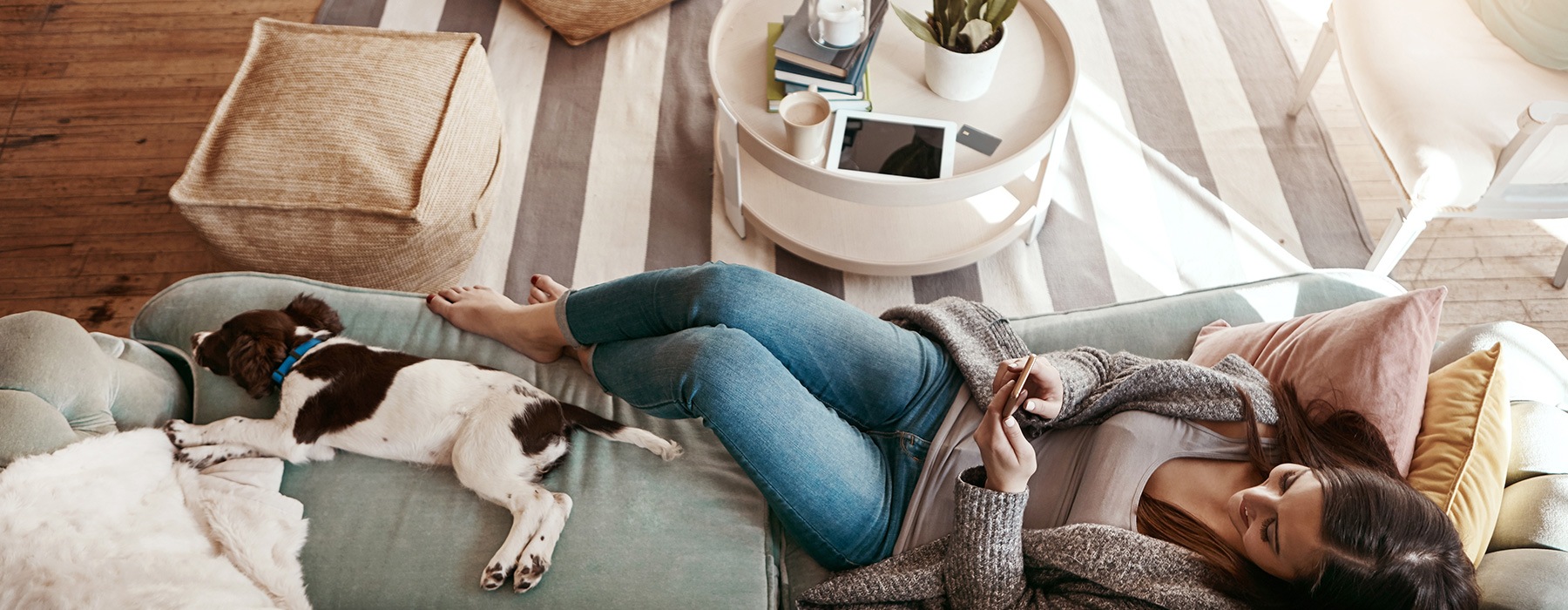 lifestyle image of a young woman laying on a couch beside her pet in a living room